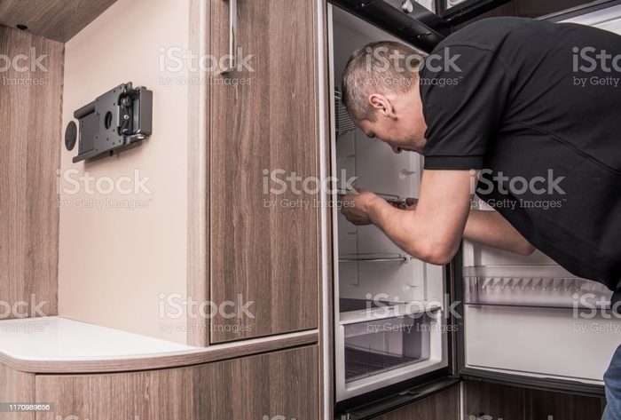 Camper Refrigerator Issue Camper Refrigerator Issue. Caucasian Technician in His 40s Replacing Motorhome Fridge. Camping and RVing Theme. Recreational Vehicle Appliances. Motor Home Stock Photo